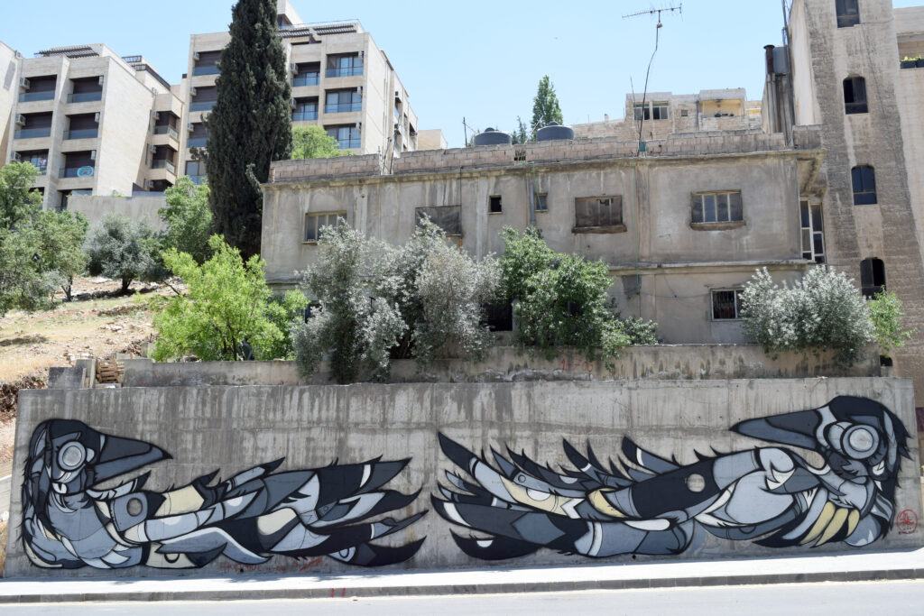 A large mural on the gable wall of a limestone building above a downtown street
